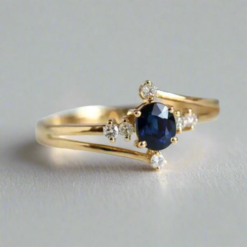 Gold ring with an oval blue sapphire centerpiece, surrounded by small diamond accents on a split gold band, inspired by celestial designs.