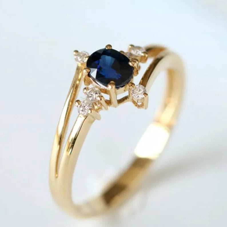 Gold ring with an oval blue sapphire centerpiece, surrounded by small diamond accents on a split gold band, inspired by celestial designs.